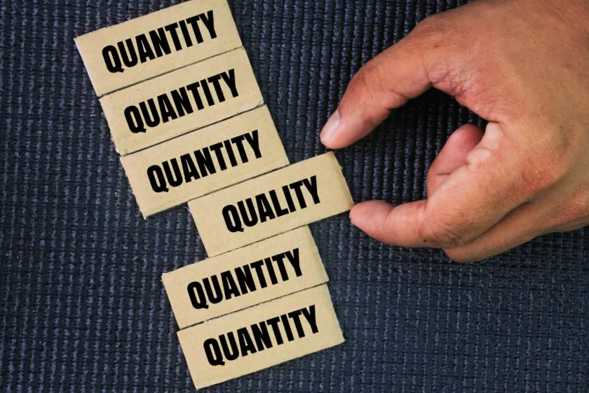 Mano colocando una tarjeta con la palabra “Quality” entre otras que dicen “Quantity”, simbolizando la importancia de la calidad frente a la cantidad en estrategias de marketing digital.