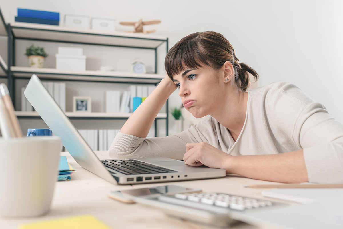 Mujer con gesto de frustración frente a su portátil por problemas digitales