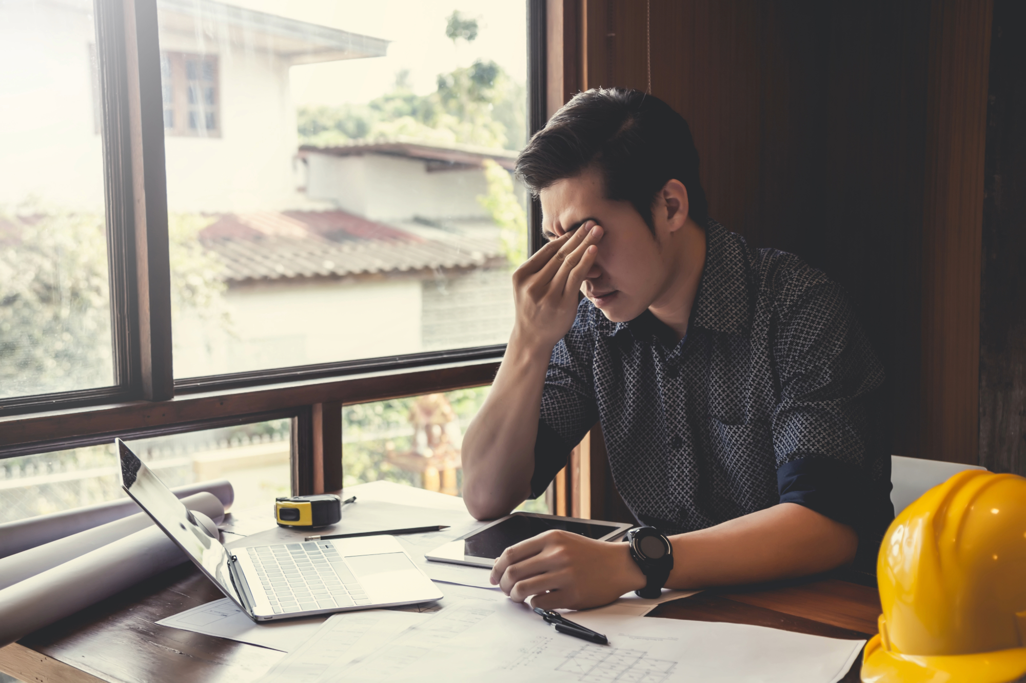 Arquitecto preocupado revisando su portfolio en el ordenador sin recibir solicitudes de proyectos.