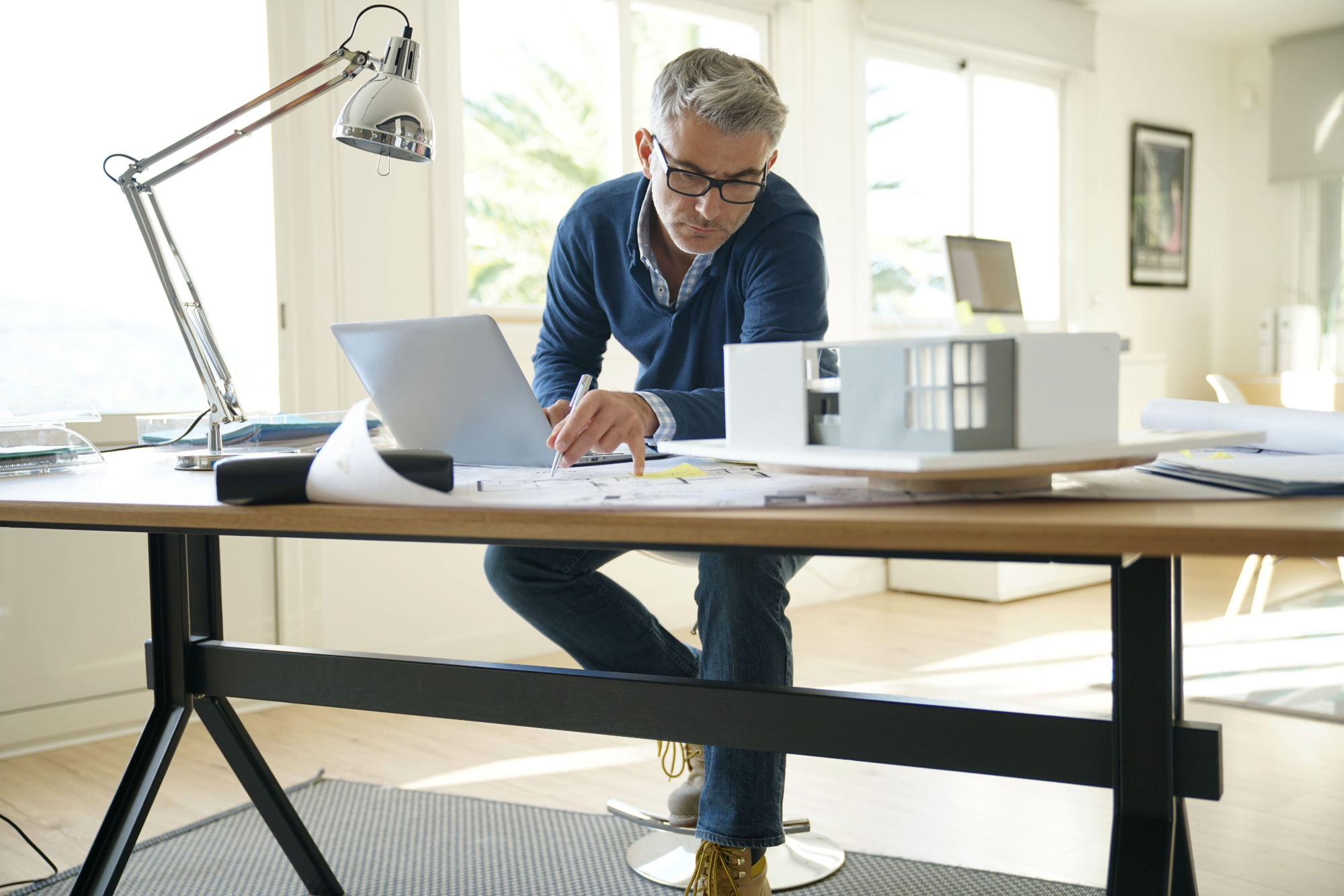Arquitecto diseñando una maqueta en su estudio con un portátil abierto junto a ella.